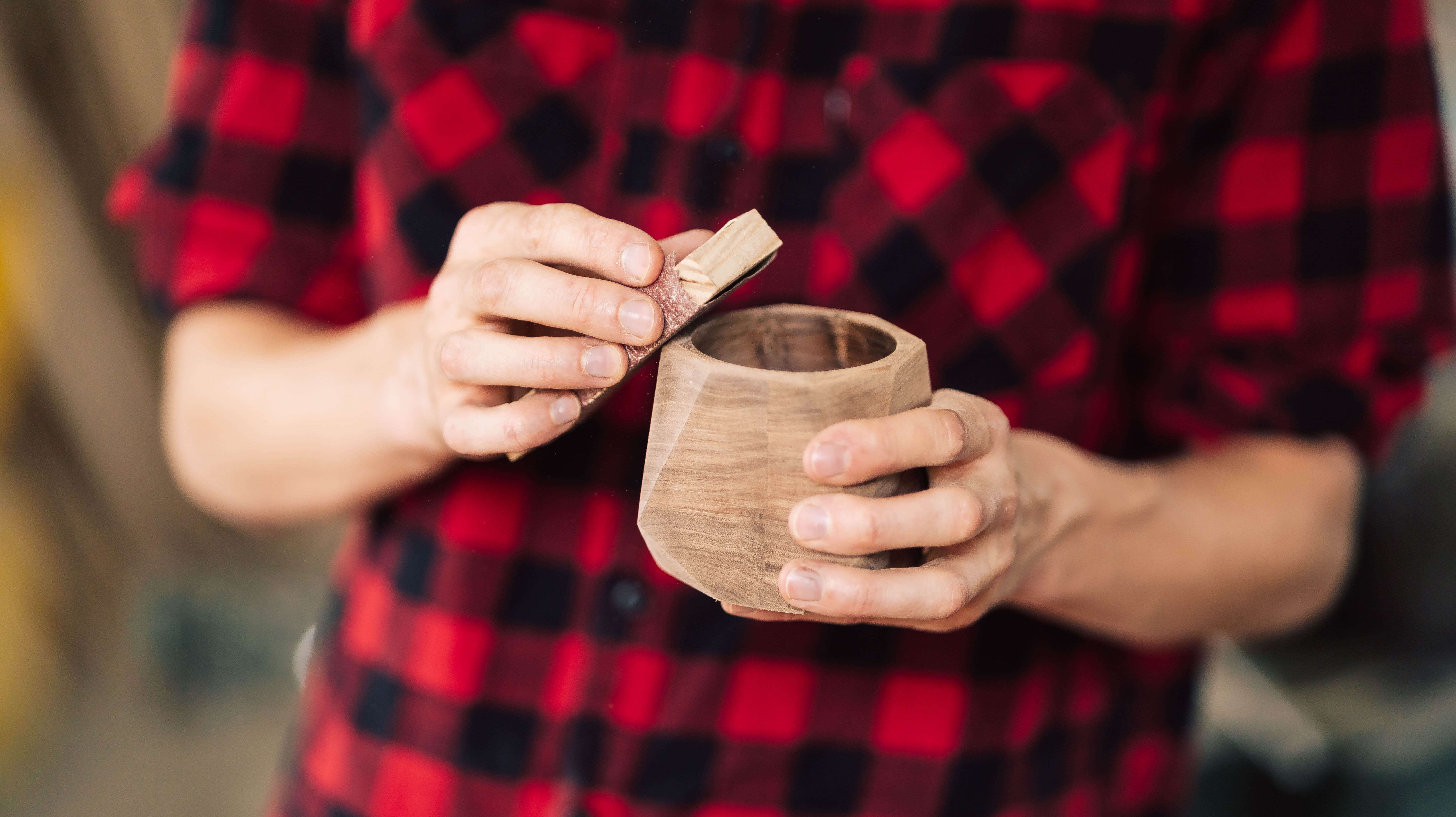 A person in a red checkered shirt holding a solid wood cup, emphasizing craftsmanship and natural materials.