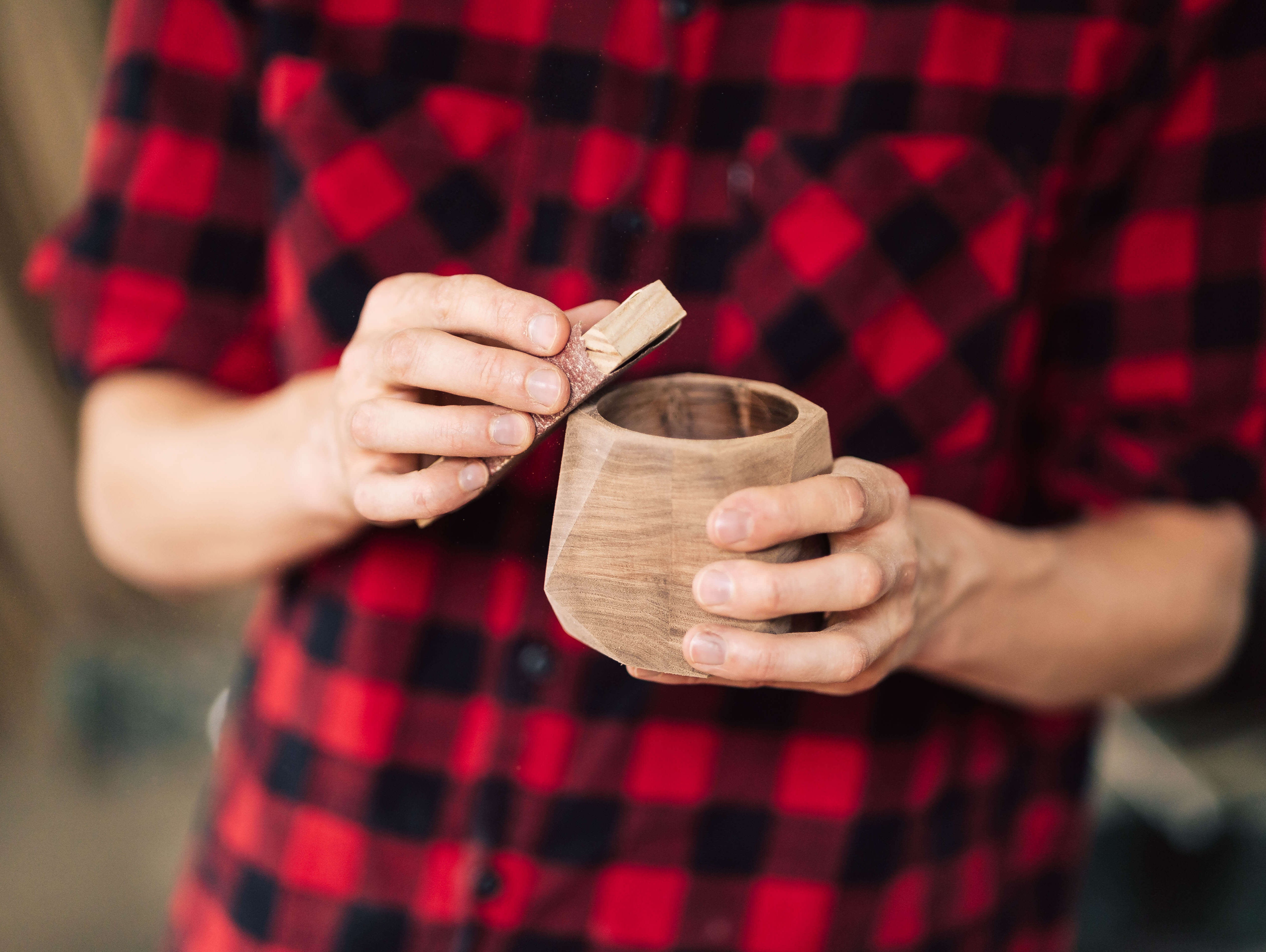 A person in a red checkered shirt holding a solid wood cup, emphasizing craftsmanship and natural materials.