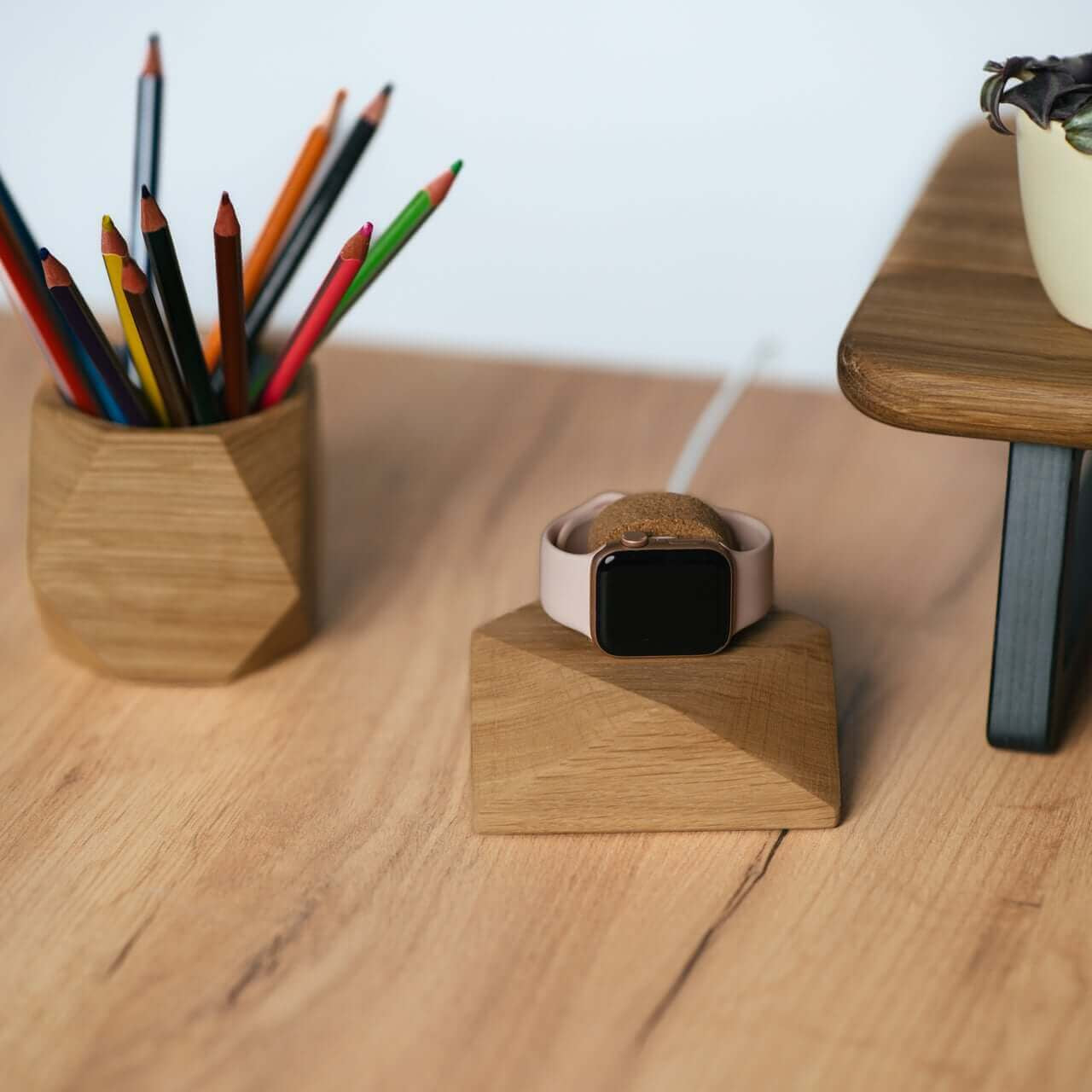 Stylish oak Apple Watch charging stand on a wooden desk with colorful pencils and a plant.