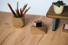 Stylish oak Apple Watch charging stand on a wooden desk with colorful pencils and a plant.