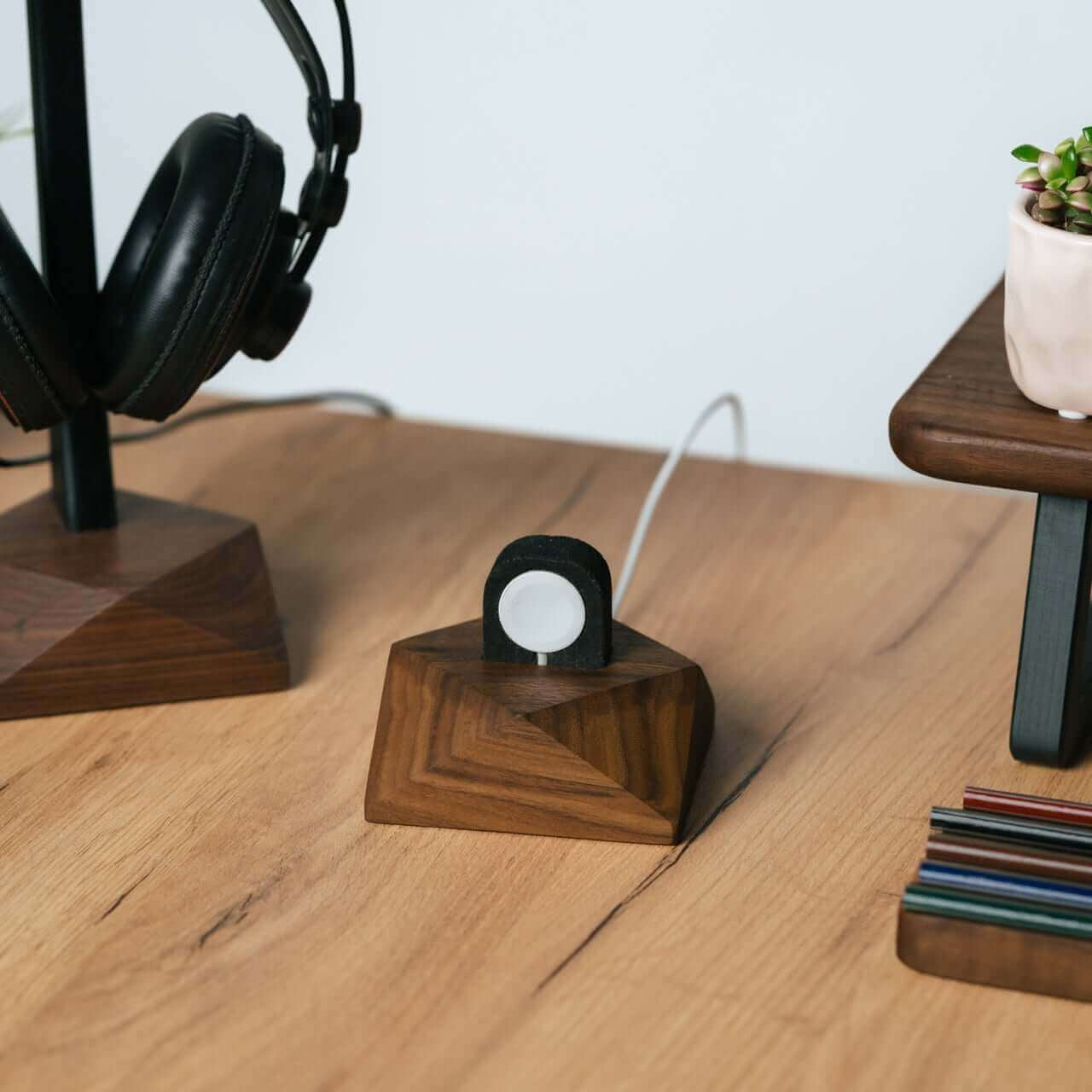 Apple Watch charging stand in walnut with headphones and succulent on a modern desk.