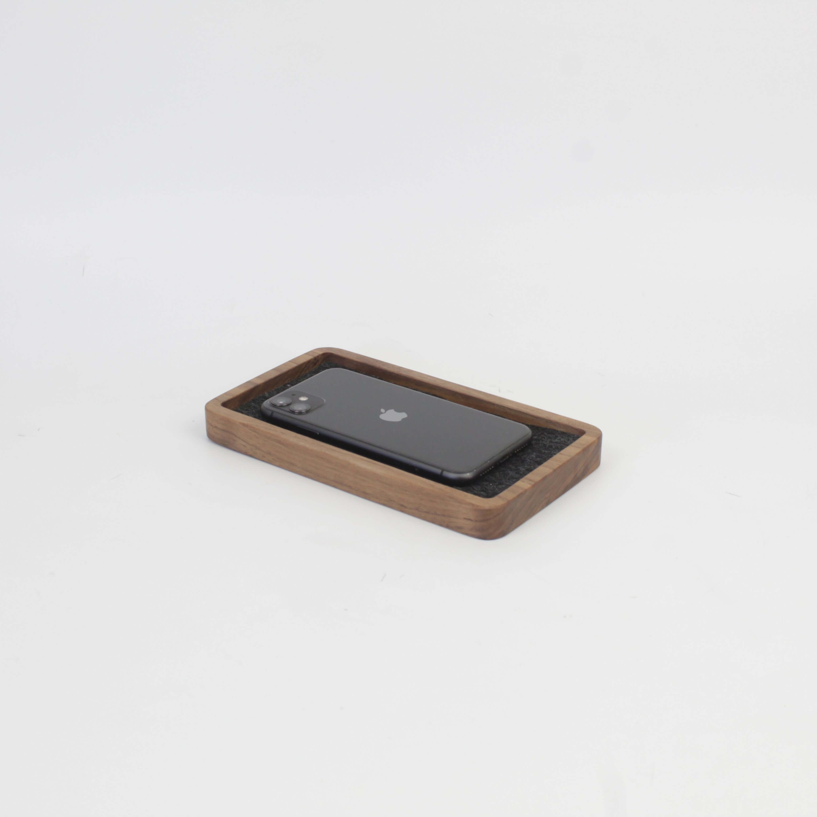 Catch all walnut tray holding a smartphone, ideal for desk organization and clutter-free spaces.
