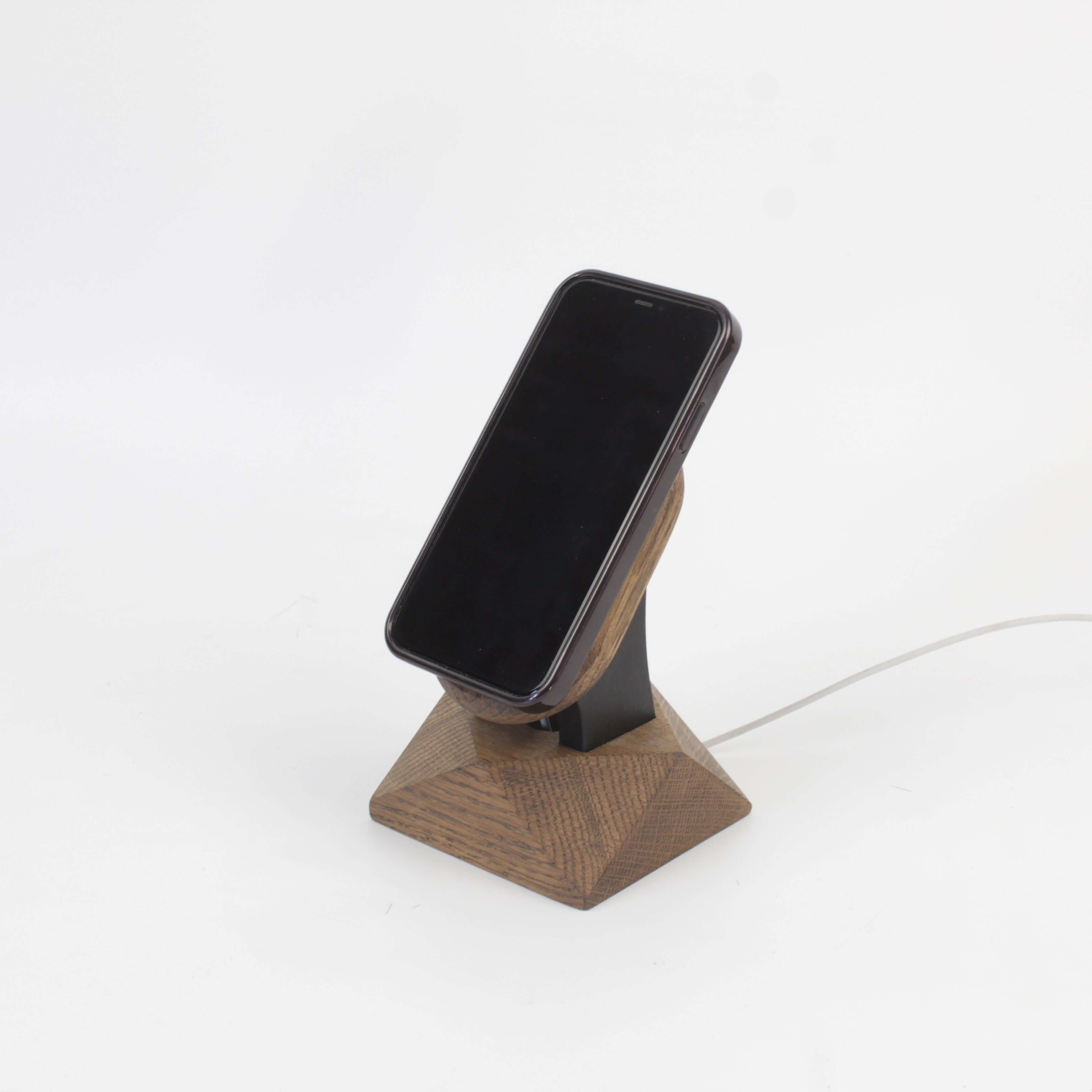 Handcrafted brown oak MagSafe stand holding an iPhone, designed for wireless charging and adding elegance to your space.