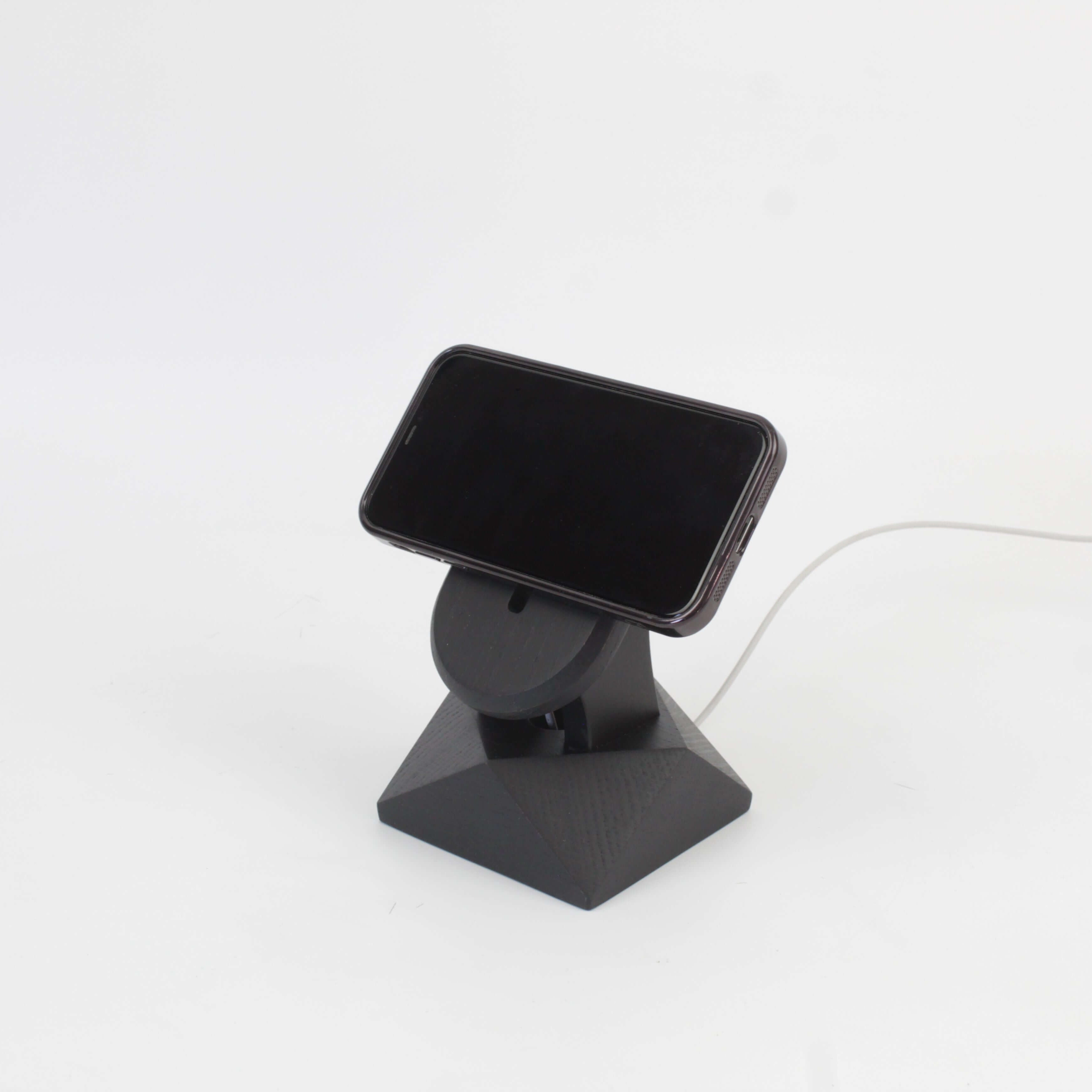 Handcrafted black oak MagSafe iPhone stand with a phone charging, showcasing modern design for iPhone accessories.