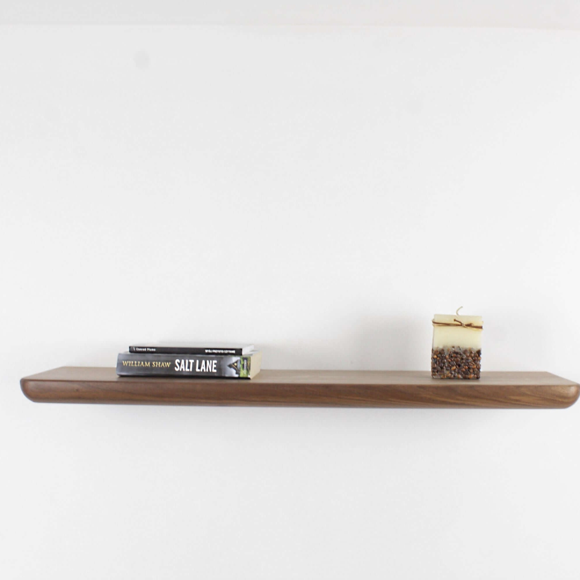 Handcrafted walnut wall shelf displaying books and a candle, perfect for modern home decor.