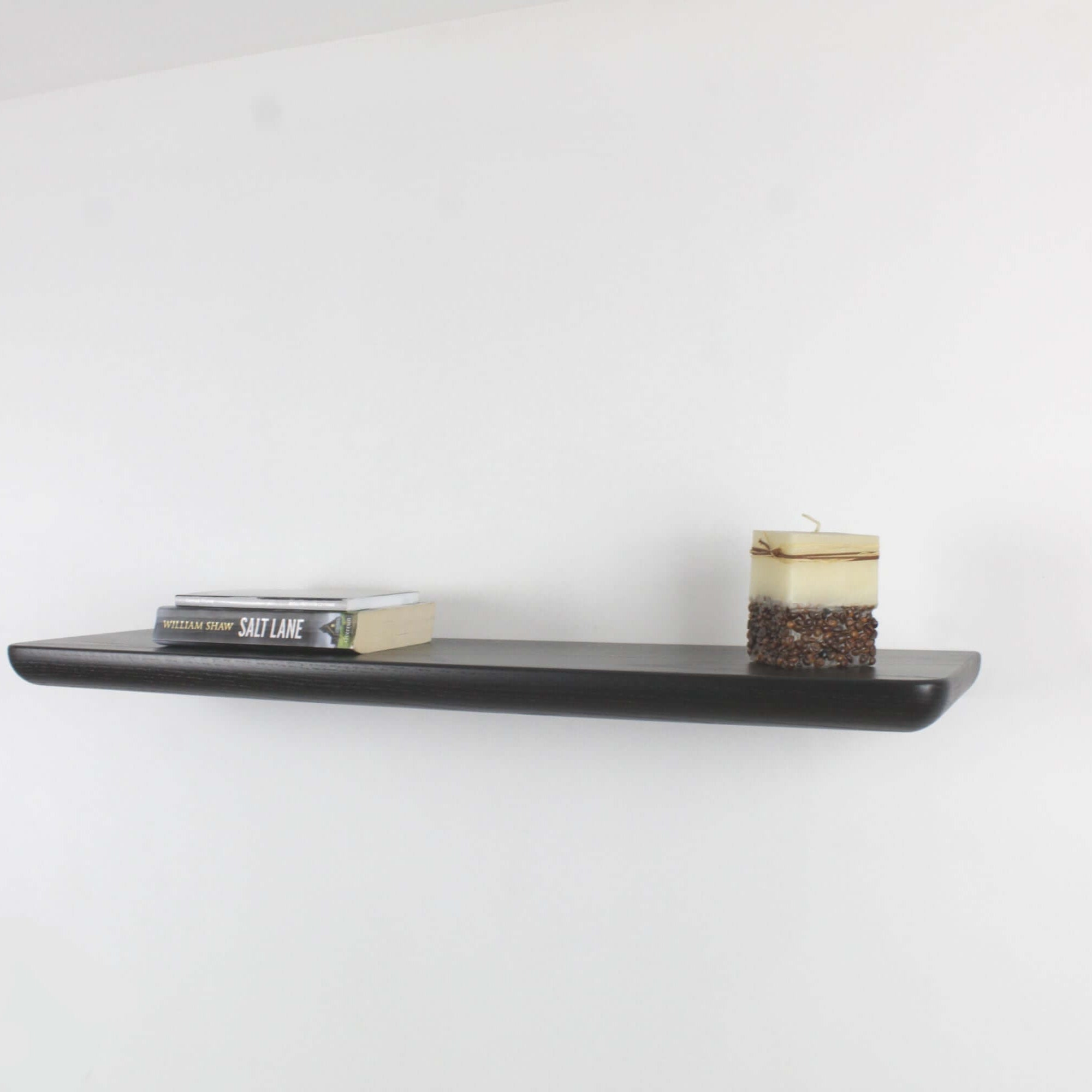 Modern black oak wall shelf displaying books and a candle, perfect for any living space or decor.