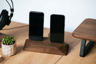 Dual phone dock in stained black oak charging two iPhones simultaneously on a clean desk with headphones nearby.