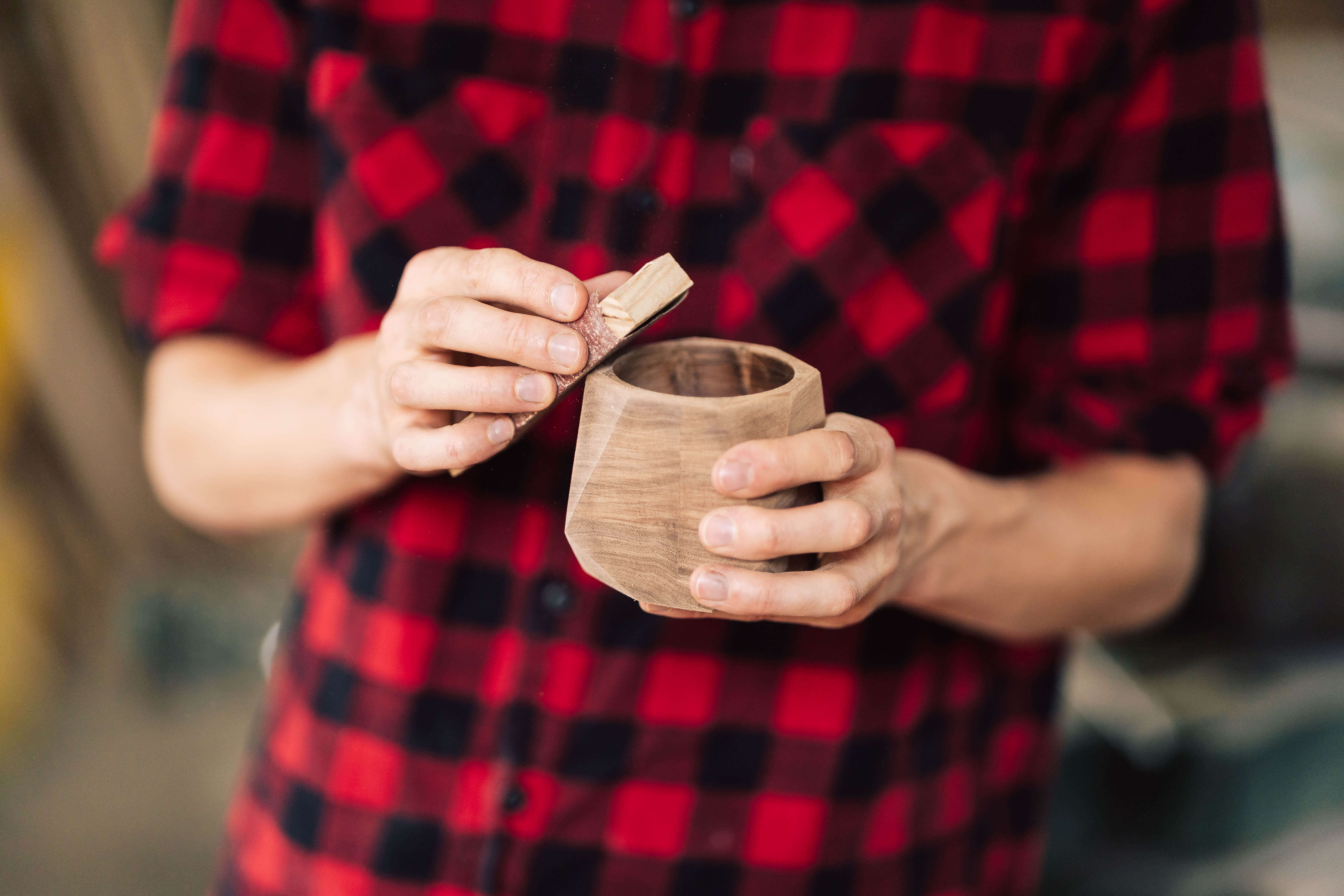 A person in a red checkered shirt holding a solid wood cup, emphasizing craftsmanship and natural materials.