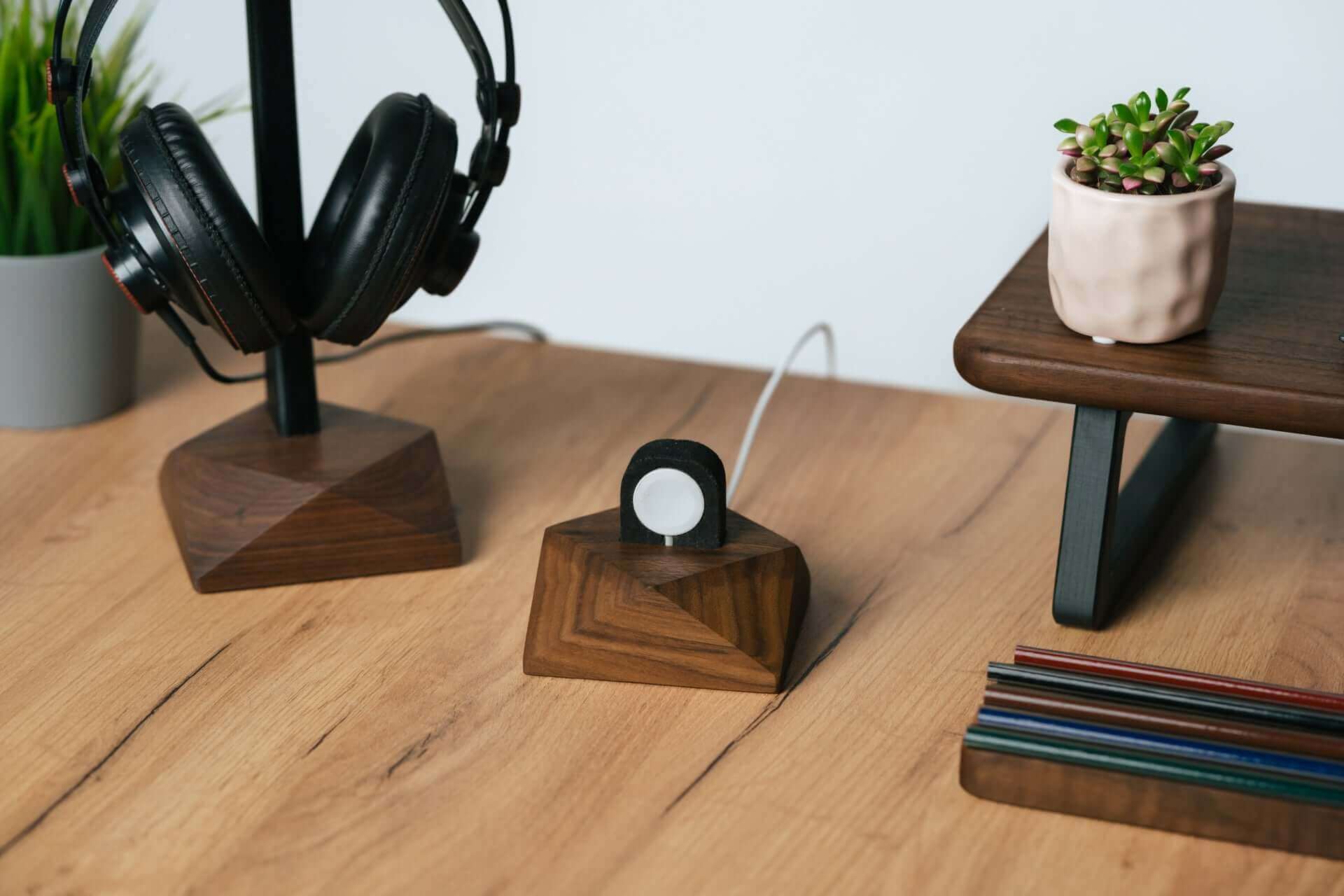 Apple Watch charging stand in walnut with headphones and succulent on a modern desk.