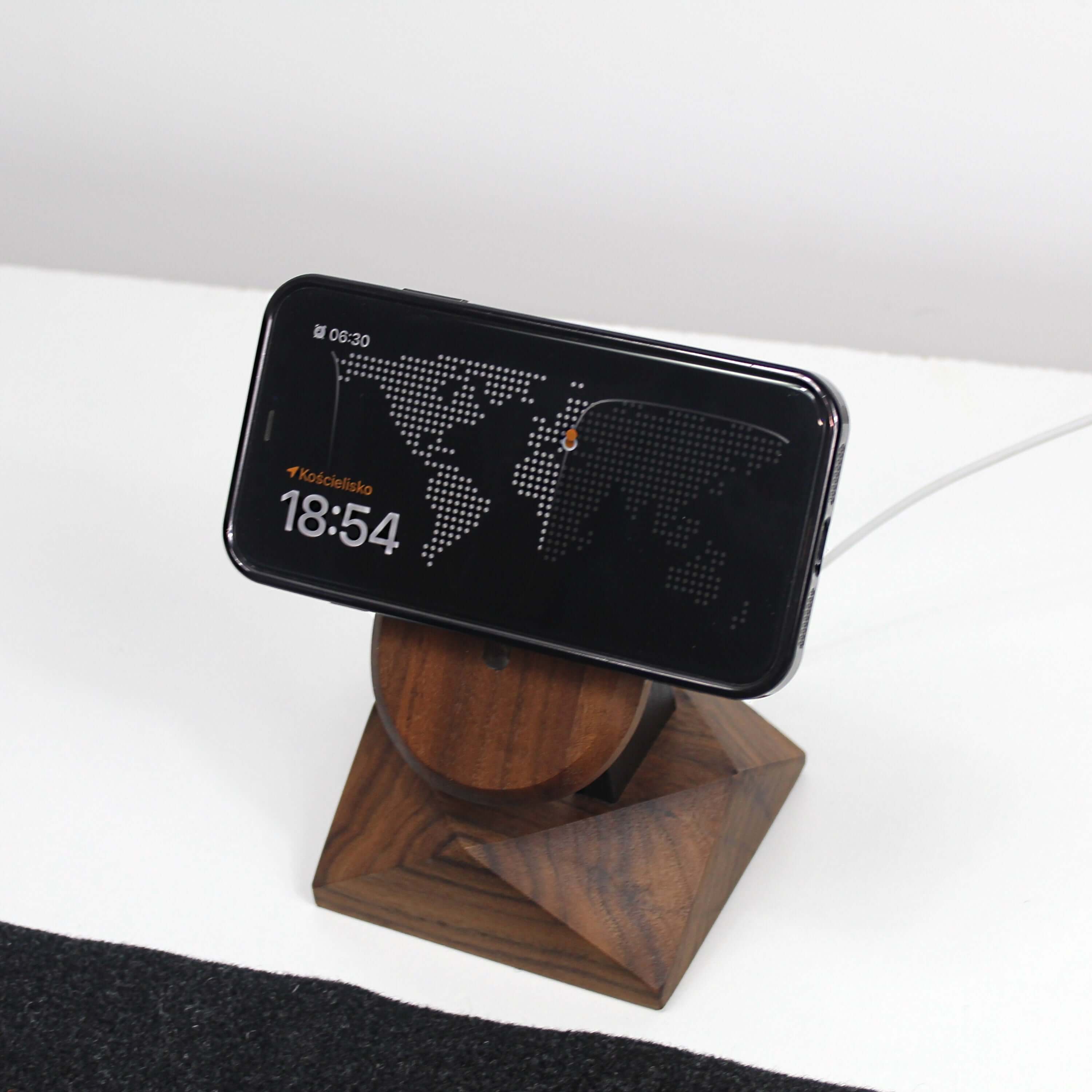 Handcrafted walnut MagSafe iPhone stand holding a wireless charger with a world map display on the phone screen.