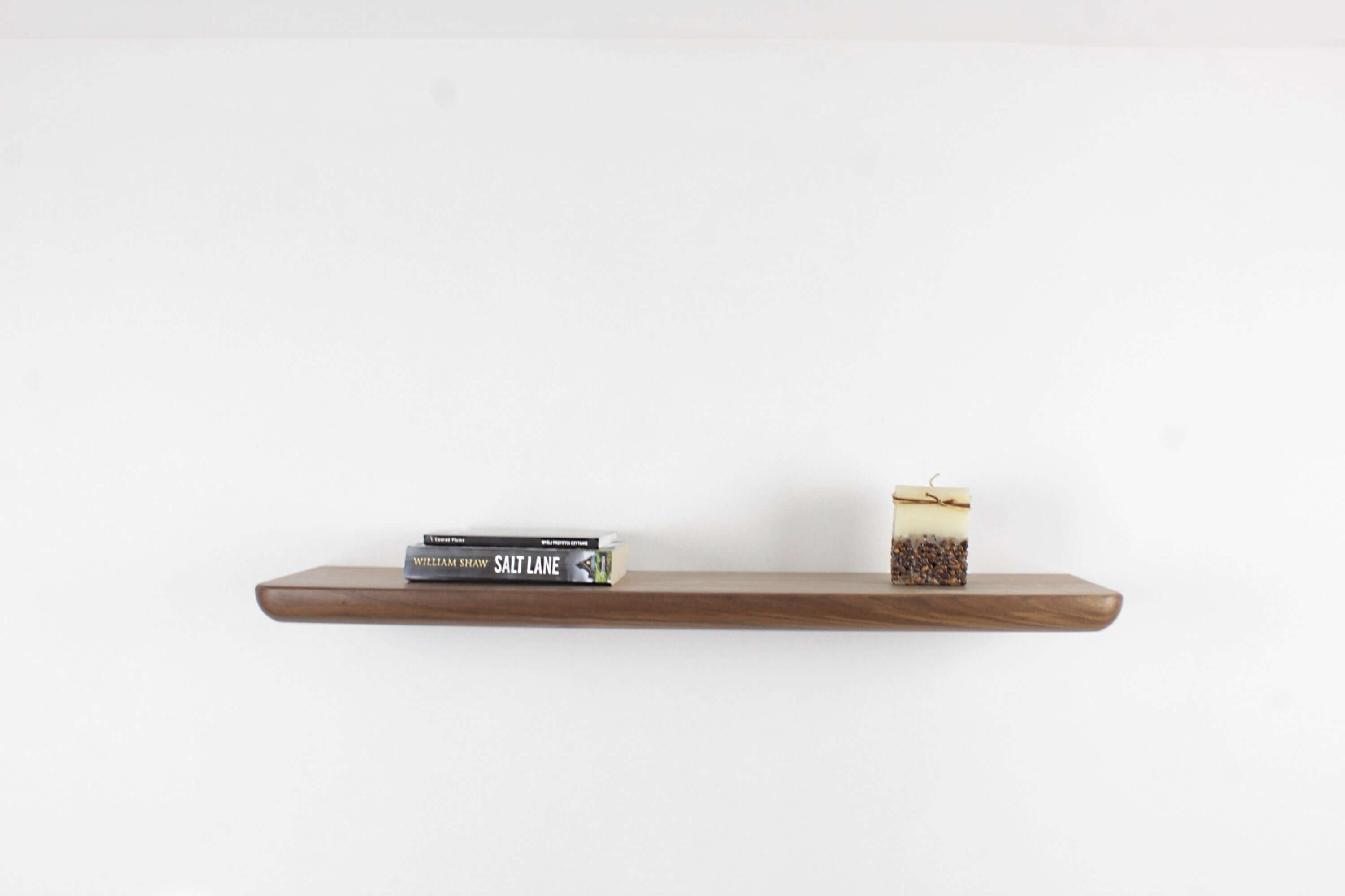 Handcrafted walnut wall shelf displaying books and a candle, perfect for modern home decor.