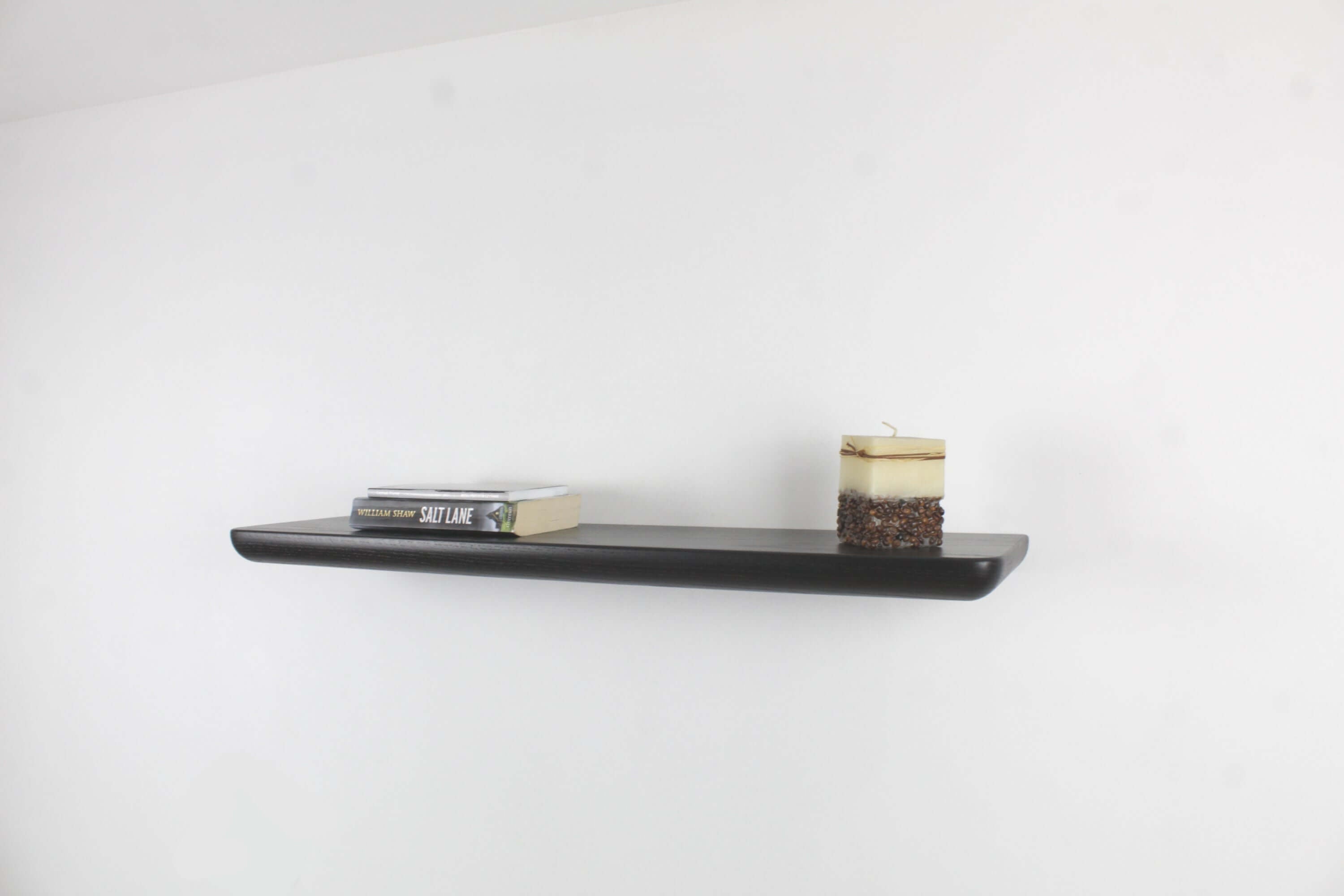 Modern black oak wall shelf displaying books and a candle, perfect for any living space or decor.